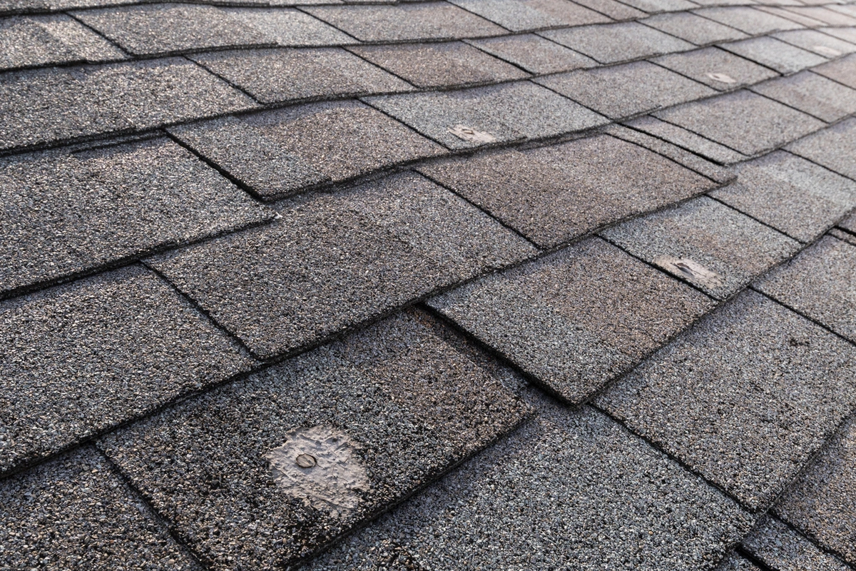 Worn asphalt shingles with lifted tabs and patches, signs guiding roof repair vs replacement decisions.
